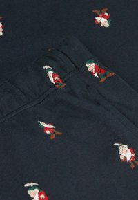 Tela azul marino con pequeños gnomos bordados en rojo, verde y marrón. Incluye una suave cinturilla elástica.