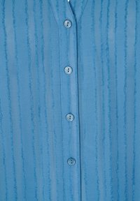 Helleblaue Bluse mit vertikalen Streifen und strukturiertem Finish, Knopfleiste vorne und rundem Kragen. Die Knöpfe sind aus matching blauem Kunststoff.