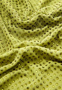 Tissu vert avec une surface texturée, arborant des gemmes jaunes brillantes uniformément réparties, créant un motif scintillant.