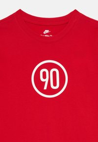 Raudona medvilninė marškinė su apvalia balta grafika, kurioje centre yra skaičius "90". Marškiniai su apvaliu kaklu, turintys lygų paviršių.