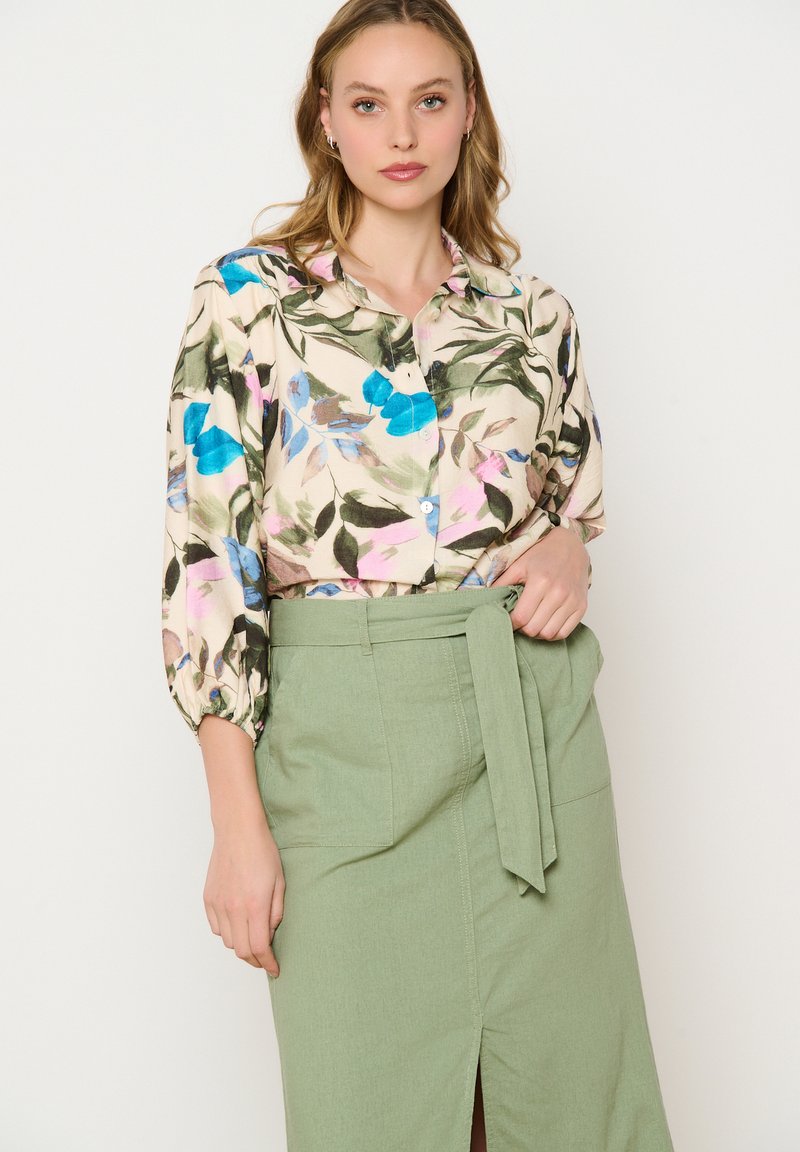 Blusa de botones con estampado floral en azul y rosa, de tela ligera, con mangas abullonadas, combinada con una falda verde de talle alto con un lazo.