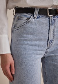 Light blue, high-waisted jeans with a slim fit, featuring denim texture, five-pocket design, and a black leather belt with a silver buckle.