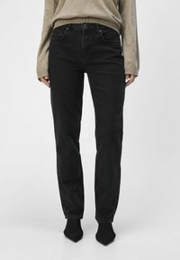 Jeans negros de pierna recta con una cintura alta, que cuentan con un diseño clásico de cinco bolsillos y un sutil acabado desgastado, combinados con un suéter beige.