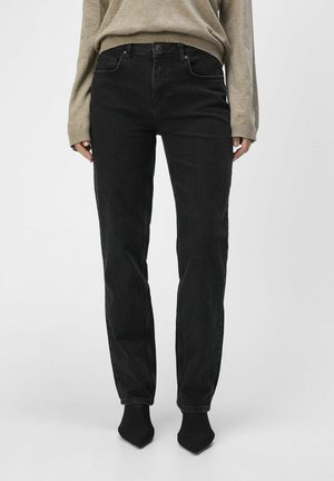 Jeans negros de pierna recta con una cintura alta, que cuentan con un diseño clásico de cinco bolsillos y un sutil acabado desgastado, combinados con un suéter beige.