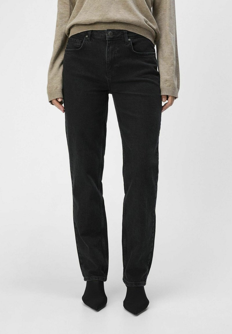 Jeans negros de pierna recta con una cintura alta, que cuentan con un diseño clásico de cinco bolsillos y un sutil acabado desgastado, combinados con un suéter beige.