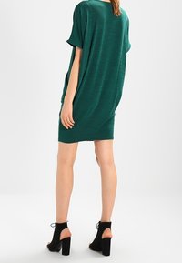 Abito verde a maniche corte con una vestibilità rilassata e una texture morbida. La modella lo abbina a stivaletti neri alla caviglia con tacco a blocco.