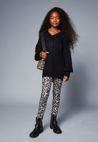 Black knitted oversized sweater with “ANV” lettering, paired with leopard print leggings and black ankle boots. The model holds a patterned bag.