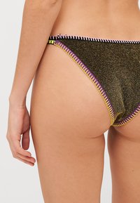 Parte inferiore di bikini nera con una finitura brillante, caratterizzata da cuciture a zigzag colorate in rosa, giallo e viola lungo i bordi.