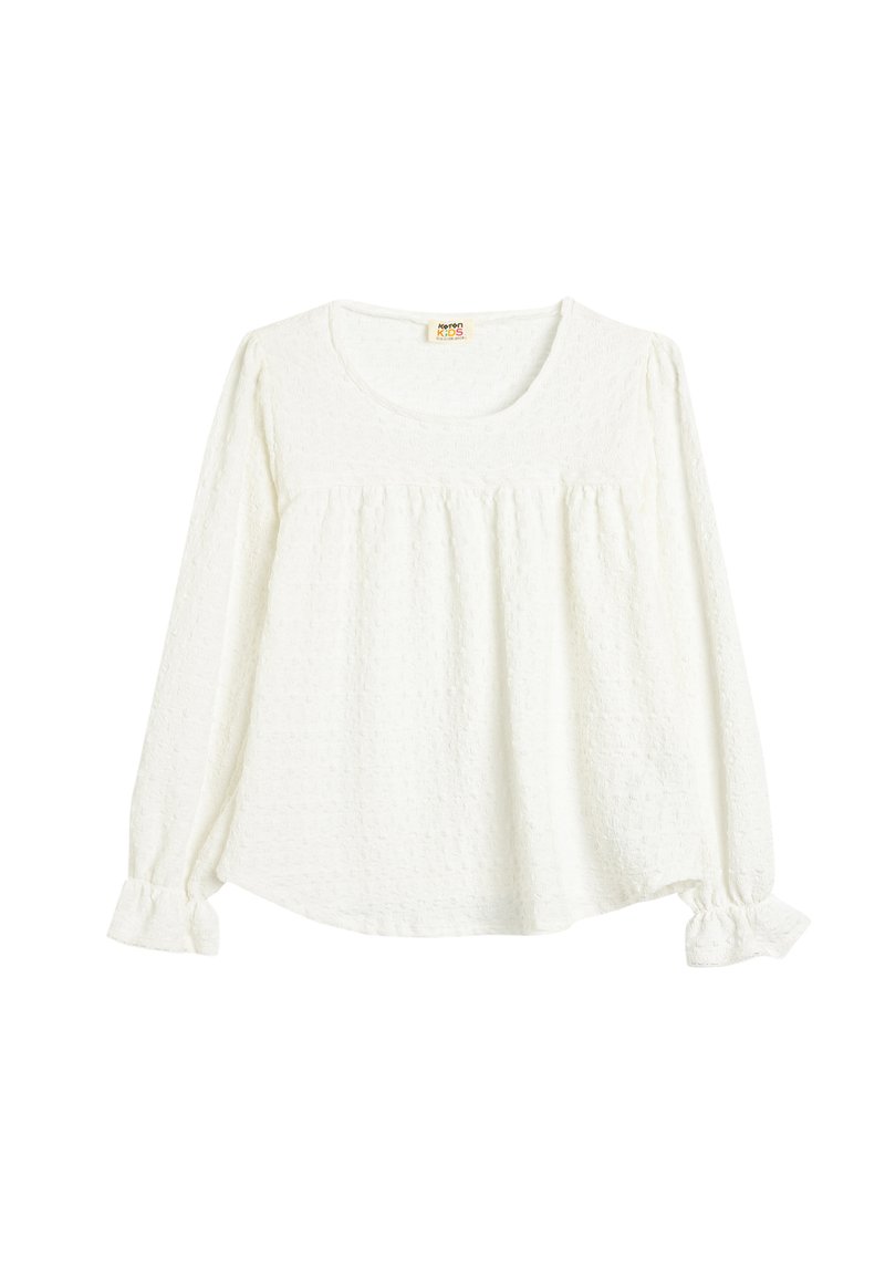 Blusa blanca de manga larga con tejido texturizado, escote redondo, cuerpo fruncido y puños con volantes. Diseño ligero y holgado.