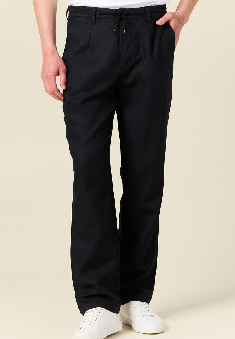 Pantaloni in lino neri con una vestibilità rilassata, caratterizzati da una vita elastica e un cordoncino. Abbinati a sneakers bianche, offrono un aspetto casual.