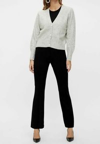 Šedý svetr s výstřihem do V, dlouhými rukávy a pěti knoflíky. Kombinováno s černými, úzkými kalhotami a černými špičatými lodičkami. Jednoduchý design.