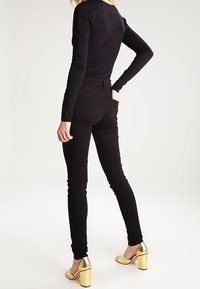 Jeans ajustados negros con una cintura alta, que presentan un diseño elegante y bolsillos traseros. Combinados con sandalias de tacón de bloque metálico dorado.
