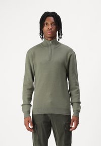 Olivengrüner, langärmliger Pullover mit Kragen und Viertelreißverschluss. Mit gerippten Bündchen und unterem Saum, aus weichem Strickmaterial.
