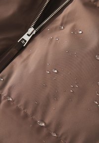 Tissu de doudoune marron déperlant avec des gouttes d'eau visibles, doté d'un zip argenté et d'une surface texturée.