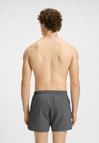 Pantaloni da bagno grigi con texture, dotati di cintura elastica e tasca posteriore, visti da dietro.