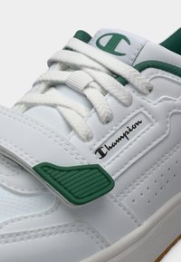 Λευκό αθλητικό παπούτσι με πράσινες λεπτομέρειες, διαθέτον ομαλή συνθετική ύλη, λουράκι στο μπροστινό μέρος, υφές και οπές για αερισμό.