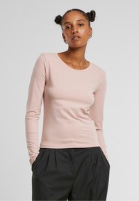 Light pink long-sleeve fitted top with a round neckline, made from a smooth fabric. Paired with black loose-fit pants.