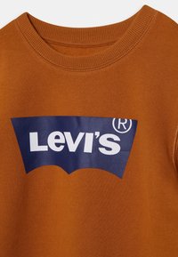 Hnědá mikina s žebrovaným výstřihem a velkým modrým logem Levi's na přední straně, které obsahuje bílý text a charakteristický zakřivený design.