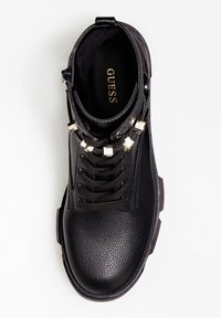 Bottines noires en cuir avec une surface texturée, un laçage, des clous carrés dorés et une semelle intérieure avec logo.