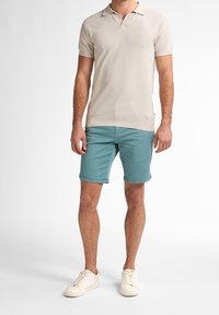 Beige kortärmad polo med texturerad tyg, matchad med teal shorts och off-white sneakers. Avslappnad sommaroutfit.