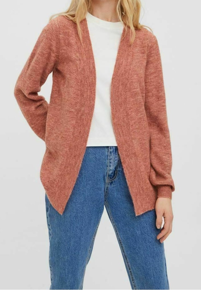 Rezavě zbarvený pletený kardigan s otevřeným předním dílem, dlouhými rukávy, žebrovanými manžetami a texturovaným povrchem, spárovaný s bílou košilí a modrými džínami.