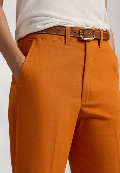 Orange trousers with a textured fabric, featuring side pockets, a brown leather belt with a gold buckle, and a tailored fit.