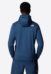 Marineblauwe hoodie met een gladde textuur, reflecterend logo op de schouder en een moderne pasvorm. Gecombineerd met bijpassende blauwe broek.