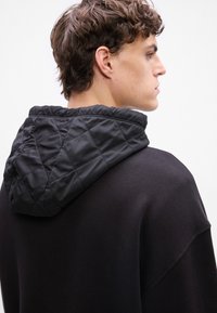 Felpa nera con cappuccio trapuntato nero. Il materiale è liscio e morbido, con un design rilassato e spalle scese.
