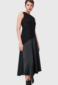 Abito nero con top a coste aderente e gonna svasata in satin. L'orlo asimmetrico e la texture liscia creano una silhouette moderna.