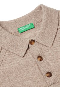 Bežová pletená polokošile s texturovaným povrchem, která má límec, tři hnědé knoflíky a zelenou etiketu "United Colors of Benetton".