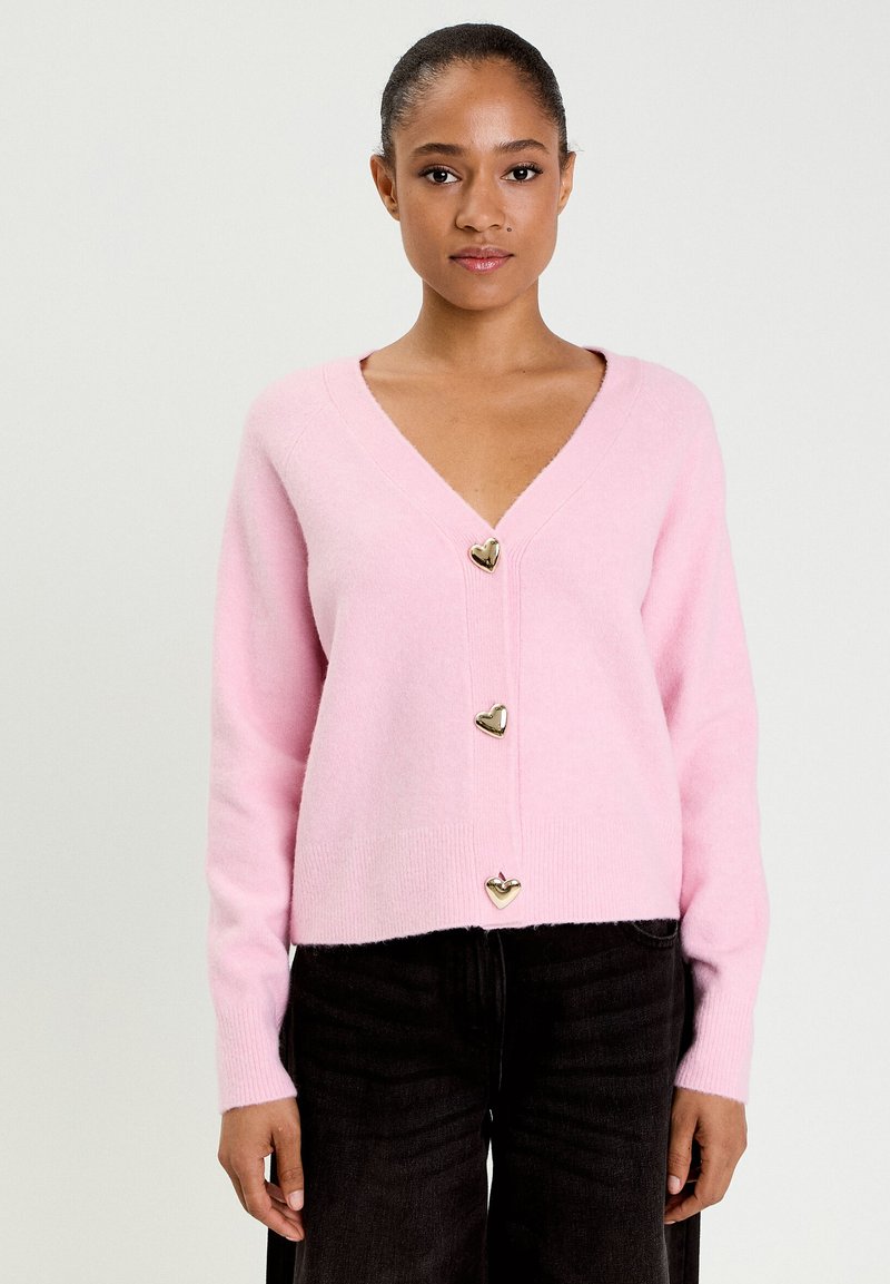 Cardigan rosa chiaro realizzato in materiale morbido, con scollo a V, maniche lunghe e tre bottoni dorati a forma di cuore lungo la parte anteriore.