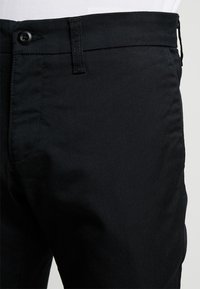 Pantaloni in cotone neri con una texture liscia, dotati di tasca anteriore, chiusura con bottone e design a gamba dritta.