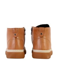 Bottes cheville en cuir tan avec une texture lisse, fermeture éclair à l'arrière, et une semelle blanche contrastante. Deux accents de matériel ronds à l'arrière.