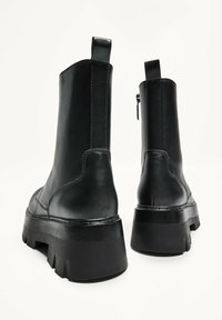 Cizme negre din piele până la glezne, cu un toc robust, textură netedă și fermoar pe lateral. Prezintă un tab pentru a fi agățat și cusături detaliate.