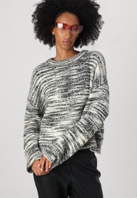 Svart og hvit stripe oversized strikkegenser med bred hals og senkede skuldre, kombinert med rødtfargede solbriller.