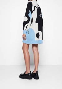 Stickad oversize-tröja med djärva abstrakta mönster i svart, vitt och ljusblått. Ribbad mudd och nederkant, tillsammans med svarta kraftiga skor.