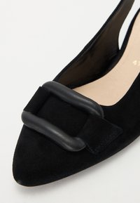 Slingbacks plats en suede noir avec un bout pointu, ornés d'une grande boucle en cuir noir mat sur le devant. Doublure intérieure lisse.