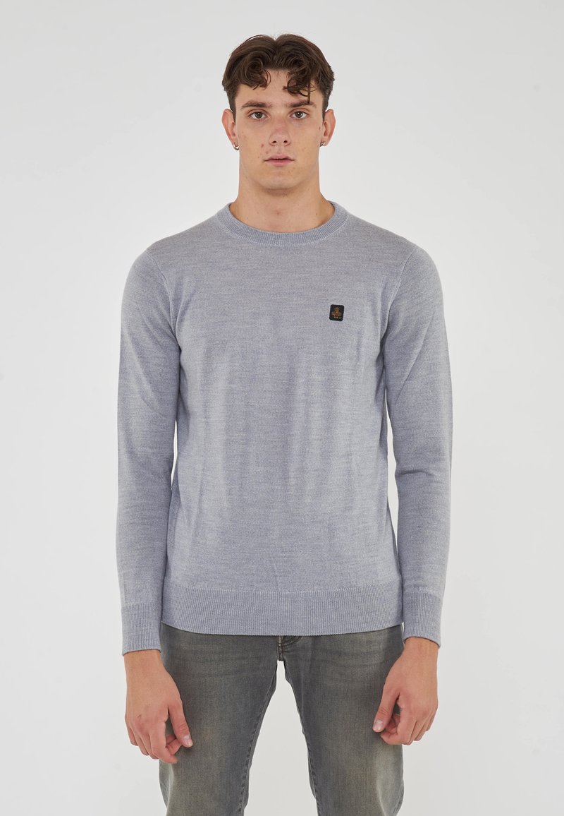 Maglione grigio chiaro a maniche lunghe realizzato in tessuto morbido, con scollo a girocollo, polsini a coste e una piccola toppa con logo scuro sul petto.