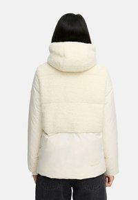 Crème jack met capuchon, voorzien van een bovenste gedeelte van nep-shearling, een gladde lagere stof en een relaxed fit. Heeft een ritssluiting en zijzakken.