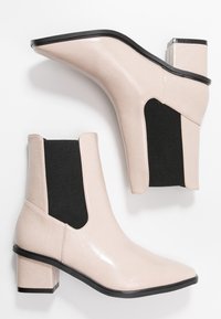 Botines de tobillo de piel sintética beige con un panel lateral elástico negro texturizado, puntera afilada y un tacón cuadrado acentuado con ribete negro.
