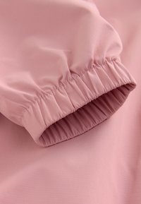 Gros plan d'une manche en tissu rose avec poignet élastique montrant des coutures froncées et une texture lisse.