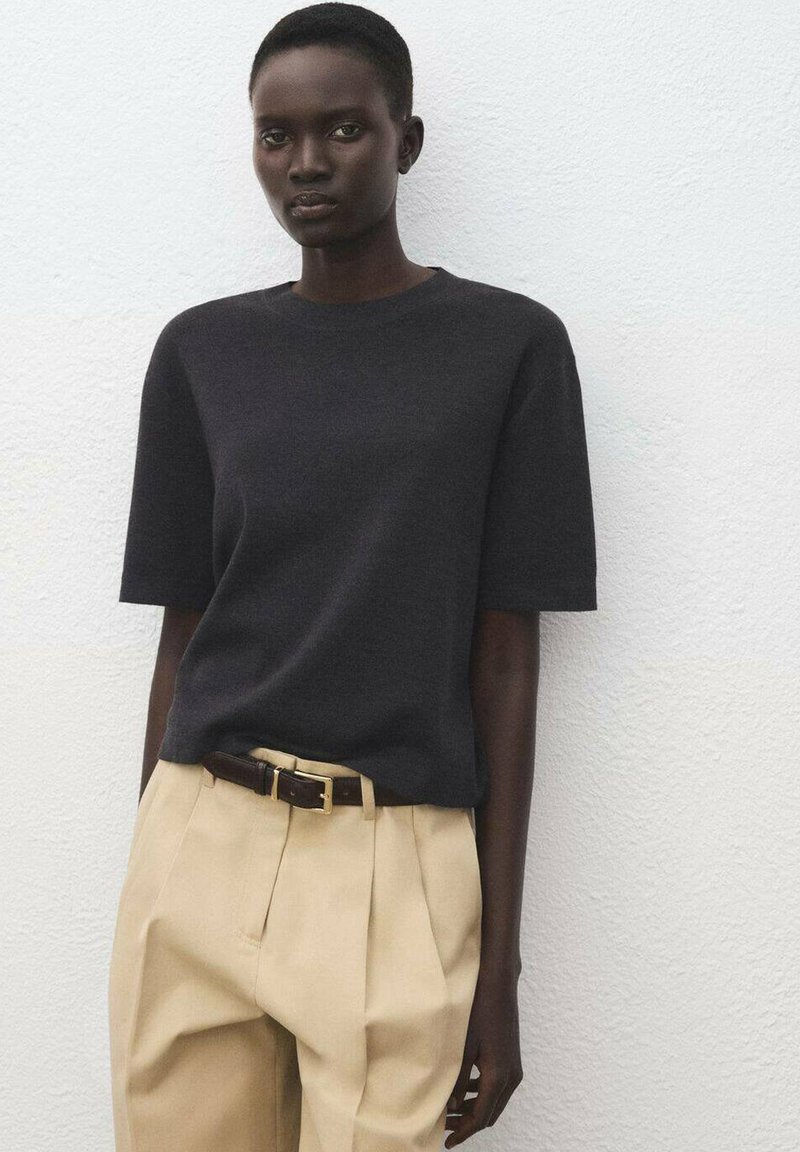 Czarny krótki top z dzianiny z krótkim rękawem zestawiony z beżowymi spodniami w wysokim stanie oraz brązowym paskiem ze złotą klamrą na jasnym tle.