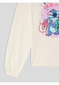 Kremowa koszula z długim rękawem, z kolorową grafiką przedstawiającą postać z kreskówki, która przytula zieloną istotę, z zabawnym napisem i gwiazdkowymi akcentami.