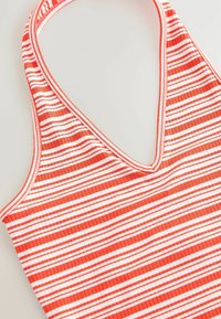 Randig halterneck-top med röda och vita vertikala ränder, ribbad textur och en djup V-ringning. Tillverkad av stretchigt material.