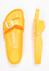 Gule Birkenstock slide sandaler med en glat overflade, justerbar rem med en sølvspænde og struktureret sål for greb. Størrelse 38.
