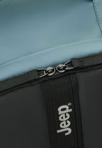 Zaino isolato blu con base in nylon nero, dotato di chiusura a doppia cerniera e logo "Jeep" argentato sulla tracolla.