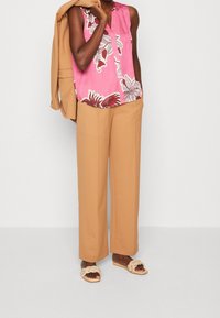 Ärmlös rosa blus med blommönster, beige vida byxor och krämfärgade flätade sandaler, vilket skapar en koordinerad outfit.