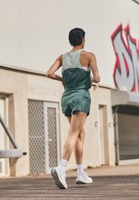 Athletic ensemble featuring a green tank top with a sheer panel, matching shorts, and white sneakers with mint accents. Smooth, lightweight fabric.