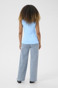 Débardeur bleu clair à côtes avec un ourlet festonné, associé à un jean large bleu clair. Modèle vu de dos avec des cheveux bouclés texturés.