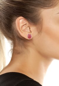 Orecchini a forma di rosa rosa realizzati in resina, con petali dettagliati e una finitura lucida. Indossati sul lobo dell'orecchio, con un design rotondo discreto.